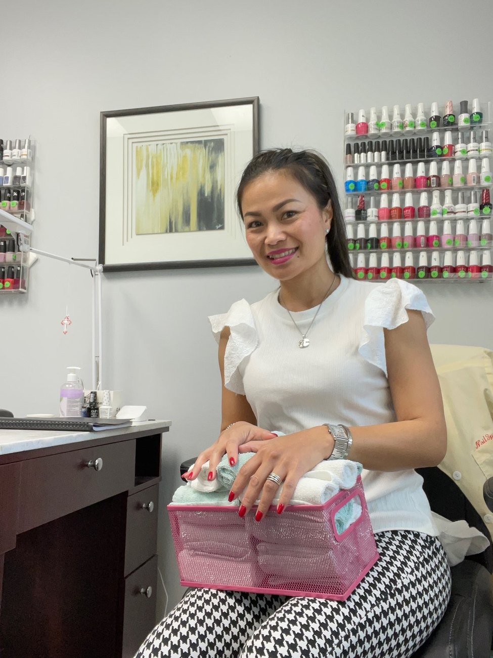 Harin, owner and nail artist at Ultimate Beauty Salon, seated by her polish wall in Durham, NC